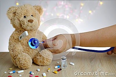 Close-up of doctor`s hand with stethoscope, many colored pills, medicine, capsules, teddy bear kids toy with stick thermometer, Stock Photo