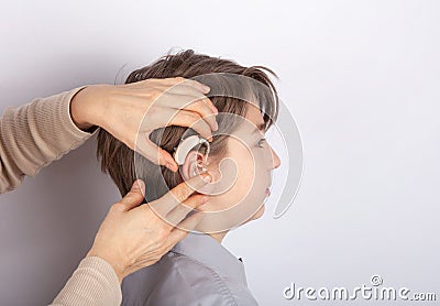 Close up of doctor`s hands inserting hearing aid in a youg boy patient`s ear Stock Photo