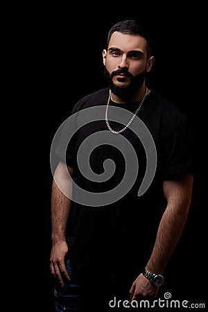 Close-up of a dramatic portrait of a young serious guy, musician, singer, rapper with a beard in black clothes on a black isolated Stock Photo