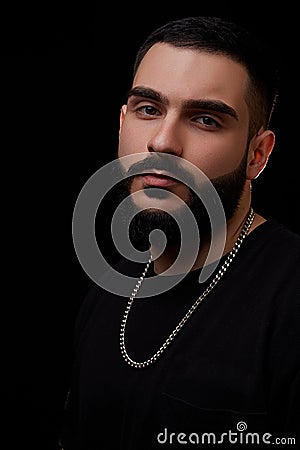 Close-up of a dramatic portrait of a young serious guy, musician, singer, rapper with a beard in black clothes on a black isolated Stock Photo