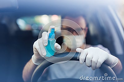 Close up of driver in protective mask with hands wearing rubber gloves on steering wheel holding alcohol sanitizer sprayer, covid- Stock Photo