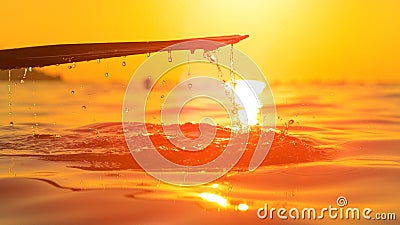 CLOSE UP: Droplets of sea water trickle off paddle illuminated by golden sunrise Stock Photo