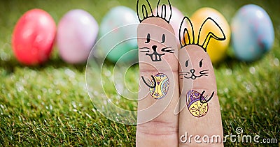 Close-up of eastern bunnies cartoon drawing on fingers against eggs on grass Stock Photo