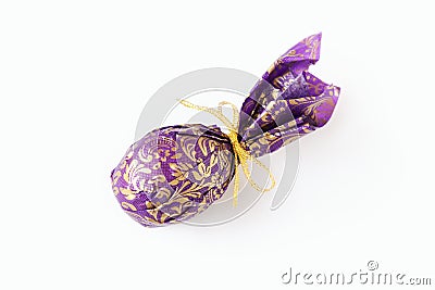 Close-up egg or ellipse shaped candy wrapped in puprle and golden paper with bow. Gift, souvenir, some sweets or traditional treat Stock Photo