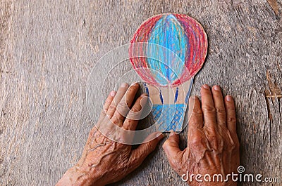 A close up of an elderly man holding a paper air baloon on a wooden table. Concept of thinking about childhood dreams, sadness and Stock Photo