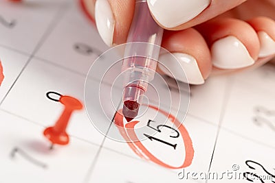 Female hand marking with a red pen on a calendar circles the 15 day, deadline concept Stock Photo