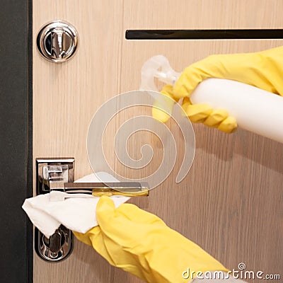 Close up entrance door knob being cleaned with sanitizer spray by female hands in yellow latex gloves, selective focus Stock Photo