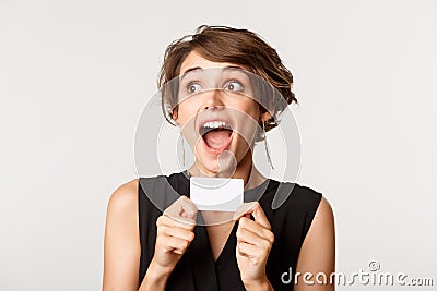 Close-up of excited young pretty woman, looking left ecstatic, showing credit card, standing over white background Stock Photo