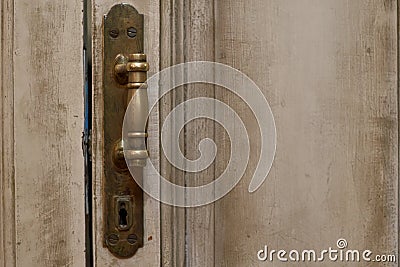Close up exterior view of an ancient wooden garage door. Metallic elements, handle and keyhole are visible. White and grey painted Stock Photo