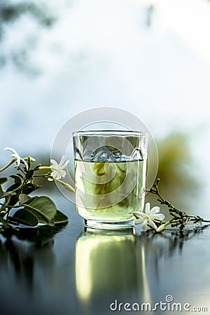 Close up of extract of Indian jasmine flower or juhi or Jasminum Auriculatum on wooden surface in a transparent glass with raw flo Stock Photo