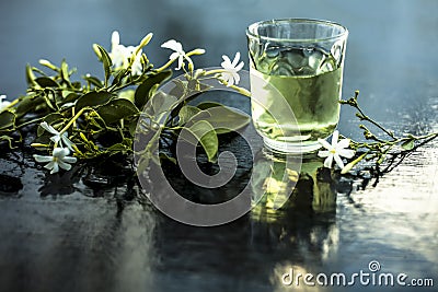 Close up of extract of Indian jasmine flower or juhi or Jasminum Auriculatum on wooden surface in a transparent glass with raw flo Stock Photo