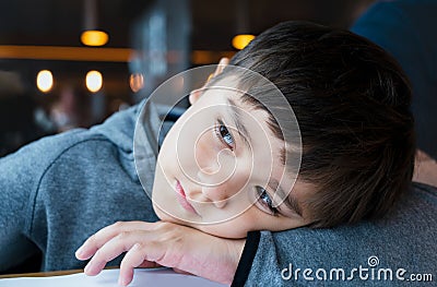 Close up face of cute little child boy lying head on hands, Candid shot mixed race kid sitting alone with smiling face looking Stock Photo