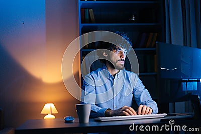 Portrait of smiling man looking intently at monitor screen while working on computer at late night. Stock Photo