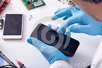 Close up faceless portrait of person`s hand in blue rubber gloves fixing damaged screen of mobile phone, unknown person sitting a Stock Photo