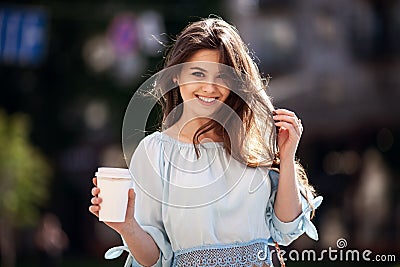 Close up fashion street style portrait of a beautiful girl in a casual outfit walks in the city . Beautiful brunette Keeps coffee. Stock Photo