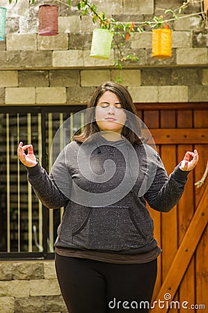 Close up of fat concentrating woman doing yoga exercise at outdoors, with both arms stretching, in a blurred background Stock Photo