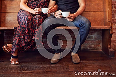 Close Up On Feet Of Couple Sitting On Bench In Coffee Shop Together Stock Photo