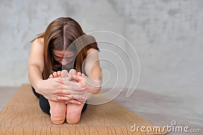 Close up on feet of naked girl practicing paschimottanasana yoga asana. Woman on forward bend pose holding hands. Flexibility Stock Photo