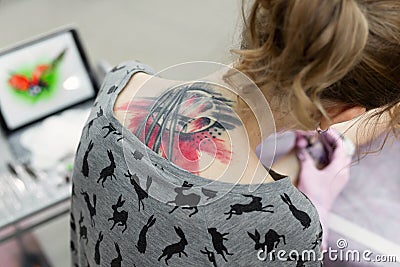 Close-up of a female artist making a color tattoo on the leg of a young girl. Rear view from the back. Stock Photo