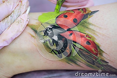 Close-up of a female artist making a color tattoo on the leg of a young girl. Tattoo artist stuffs a ladybug on a Stock Photo