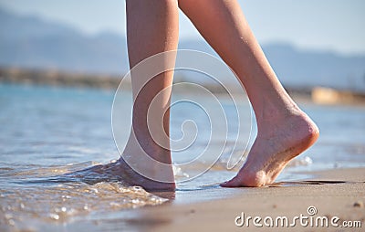Close up of female feet walking barefoot on white grainy sand of golden beach on blue ocean water background Stock Photo