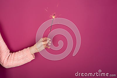 Close up of female hand with burning Christmas sparkler on pink background. Copy space Stock Photo