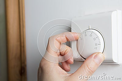 Close Up Of Female Hand On Central Heating Thermostat Stock Photo