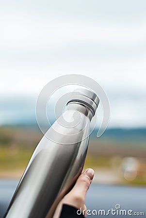 Close-up of female hand holding a steel reusable thermal water bottle on background of sky. Stock Photo