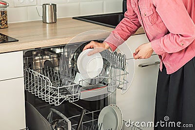 Close-up of female hand loading wished to, empty out or unloading from open automatic built-in dishwashers machine with clean Stock Photo