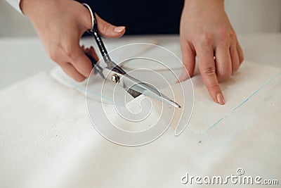 Close-up female hands cuts out a piece of fabric on which a chalk pattern of clothing is marked for tailors Stock Photo