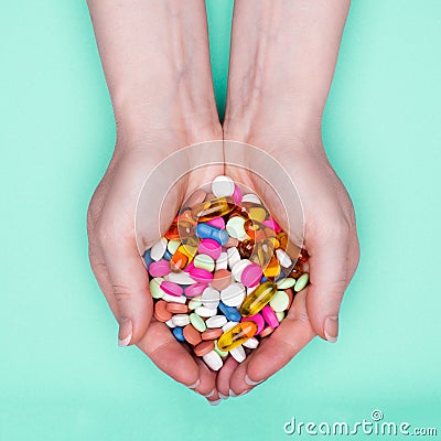 Close up of female hands holding heap of colorful medication pills over pastel blue background. Stock Photo