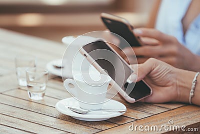 Close-up of female hands holding phones chatting on social network or shopping online in cafe with two cups of coffee Stock Photo