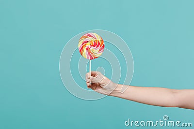 Close up female holding in hand colorful round lollipop isolated on blue turquoise wall background. Proper nutrition or Stock Photo