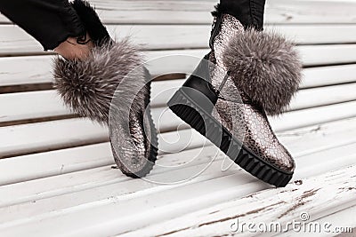 Close-up of female legs in a glamorous stylish silver sneakers with gray fur. Modern young woman in jeans in fashionable winter Stock Photo