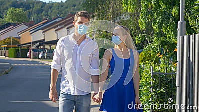 CLOSE UP: Girl looks into boyfriends eyes as they walk down street wearing masks Stock Photo