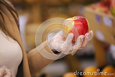 Close-up of females hand in protective gloves hold beautiful fresh apple in hand. Shopping during quarantine Stock Photo