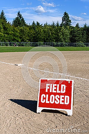 Close up of Field Closed sign on empty local baseball field, third base and baseline, on a sunny day with woods and blue sky in th Stock Photo