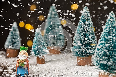 Close-up of figure of the Magus King Melchior with artificial Christmas trees, snow falling, on wooden table with snow, selective Stock Photo
