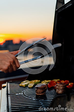 Close-up of filet mignon vegetables and meat on a bbq grill on a skyscraper rooftop at sunset. Fire in the barbecue Stock Photo