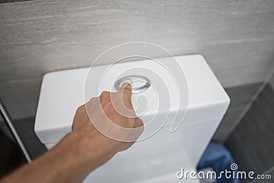 Close up of finger pushing a flush toilet button for cleaning a toilet. Stock Photo