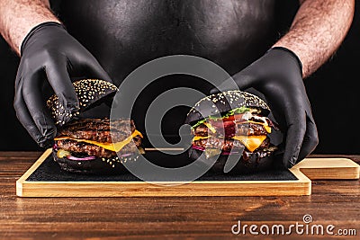 Close-up, finishing touch preparing a grilled burger. Chef holds in his hand a grilled burger with a black bun Stock Photo