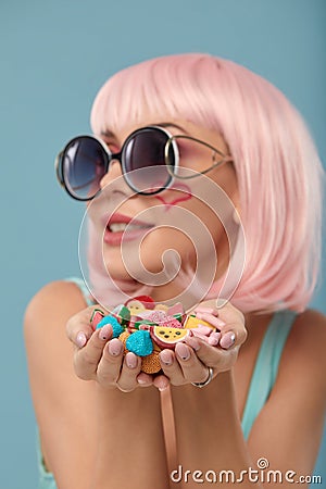 Close up of a flirtatious female model on blue background wearing a pink wig holding different kinds of candies. Pretty Stock Photo