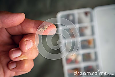 Close up of fly fishing fly on the finger next to box with tied flies. Fly fishing equipment still life Stock Photo