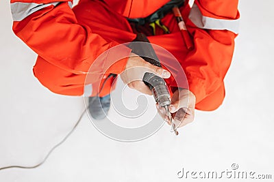 Close up foreman in orange work clothes holding drill machine in Stock Photo