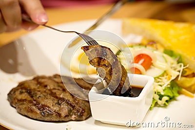 Close up the fork pick up beef steak and dipped in barbecue sauce. Stock Photo