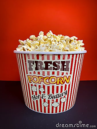 Close up fresh buttery popcorn in a stripped red and white bowl on red background Stock Photo