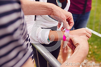 Close Up Of Friends At Entrance To Music Festival Putting On Security Wristbands Stock Photo