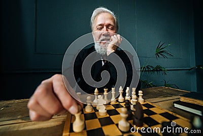 Close-up front view of positive bearded mature male performing move with pawn piece on wooden chessboard. Stock Photo