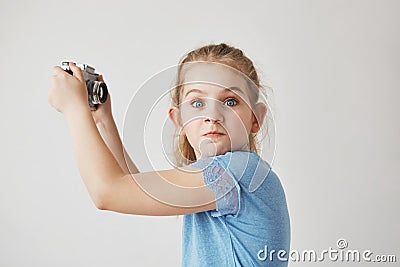 Close up of funny blonde girl in blue shirt holding camera in hands,going to make selfie when her friend starts to Stock Photo