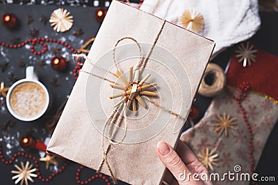 Close-up of the girl holding a homemade gift box of Kraft paper on the background of Christmas table Stock Photo